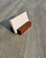 A small wooden business card holder made of two wood tones, holding blank white cards, set on a gray wood-grain tabletop.