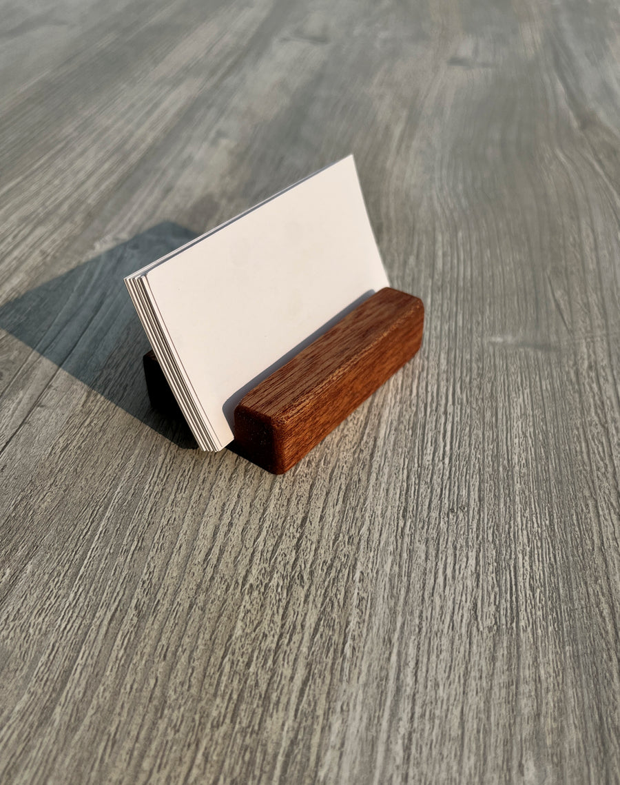 A small wooden business card holder made of two wood tones, holding blank white cards, set on a gray wood-grain tabletop.