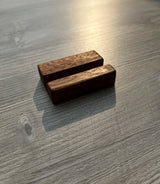 Small rectangular dark brown wooden business card holder with visible grain, placed on a gray wood-textured surface with warm sunlight and shadows.