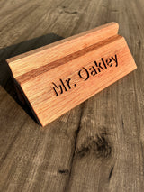 A personalized wooden desk nameplate engraved with 'Mr. Oakley', made from warm medium-brown wood and resting on a rustic dark wood tabletop.