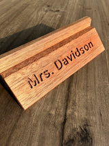 A personalized wooden nameplate stand engraved with 'Mrs. Davidson', shown on a rustic wood tabletop.