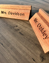 Two personalized wooden name signs, one engraved with 'Mrs. Davidson' and the other with 'Mr. Oakley'