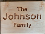 A personalized wooden sign engraved with the text 'The Johnson Family' in a warm light wood tone.
