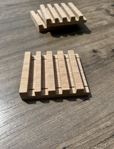 Three rectangular wooden slatted soap dishes with a natural light wood finish, displayed on a dark wood tabletop.