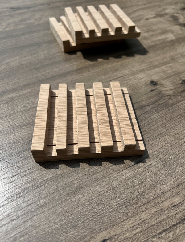 Three rectangular wooden slatted soap dishes with a natural light wood finish, displayed on a dark wood tabletop.