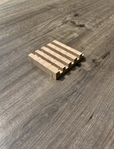 A small rectangular soap dish with five parallel grooves, photographed on a gray wood-grain surface.