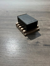 A small black rectangular bar of soap placed on a wooden soap dish, placed on a gray wood-grain surface.